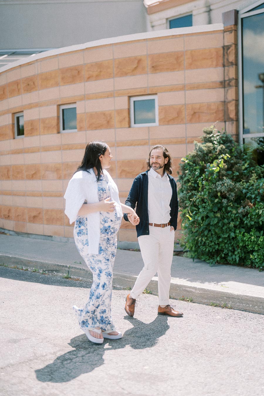 Expectant couple holding hands while walking outside a stone building