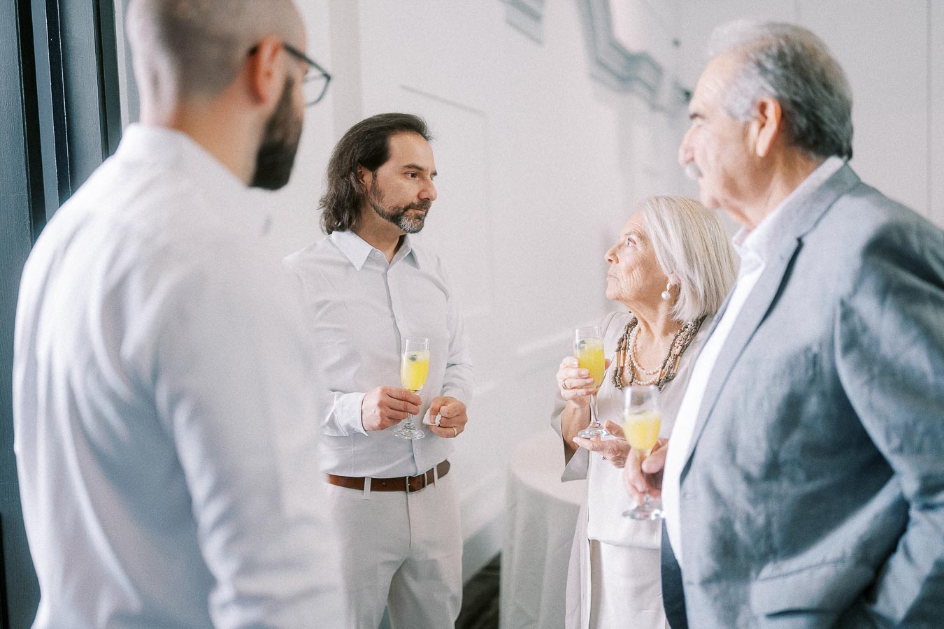 Guests in formal attire holding orange drinks during a bright indoor reception