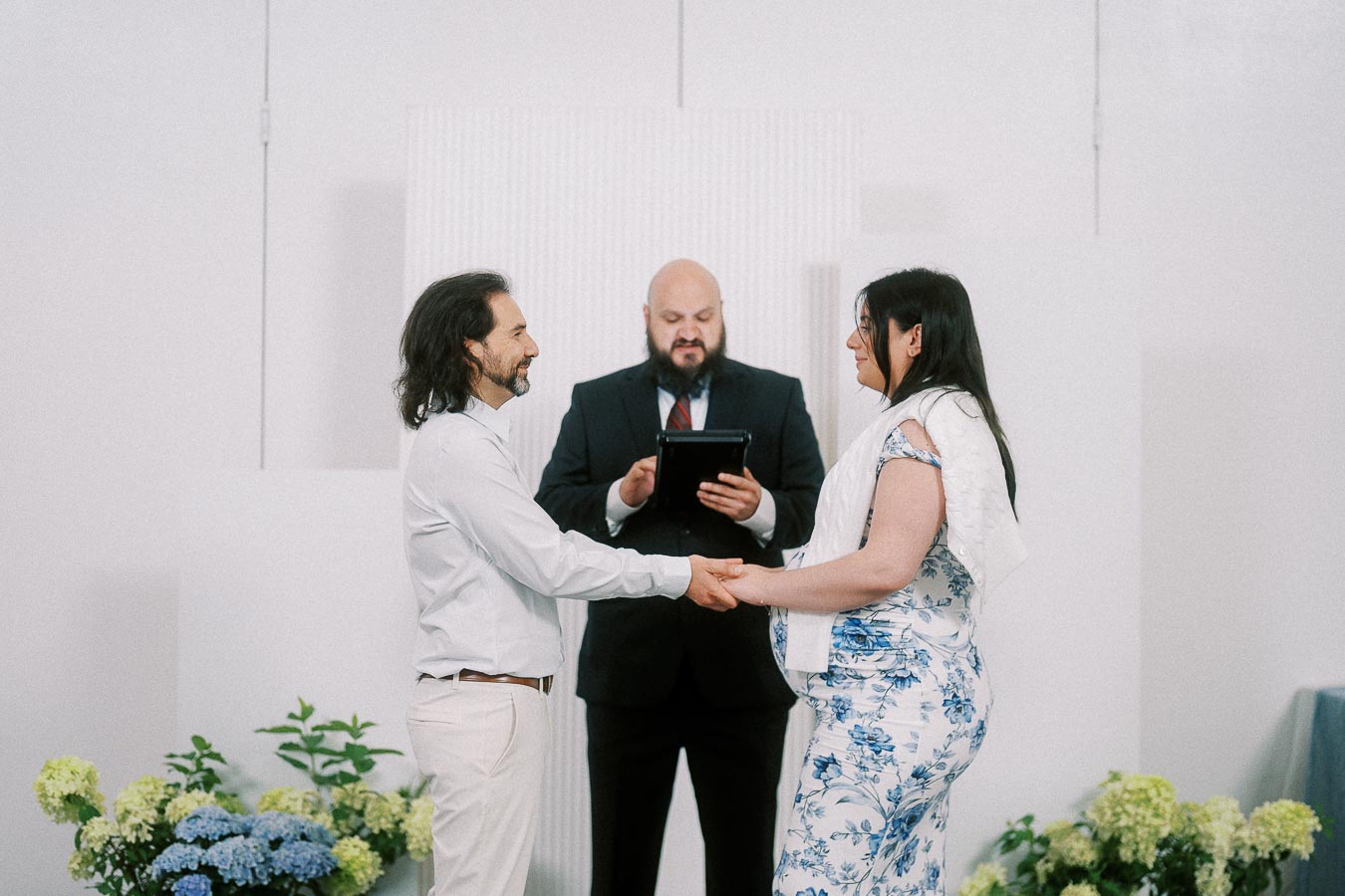 Couple holding hands during a ceremony with officiant reading from tablet