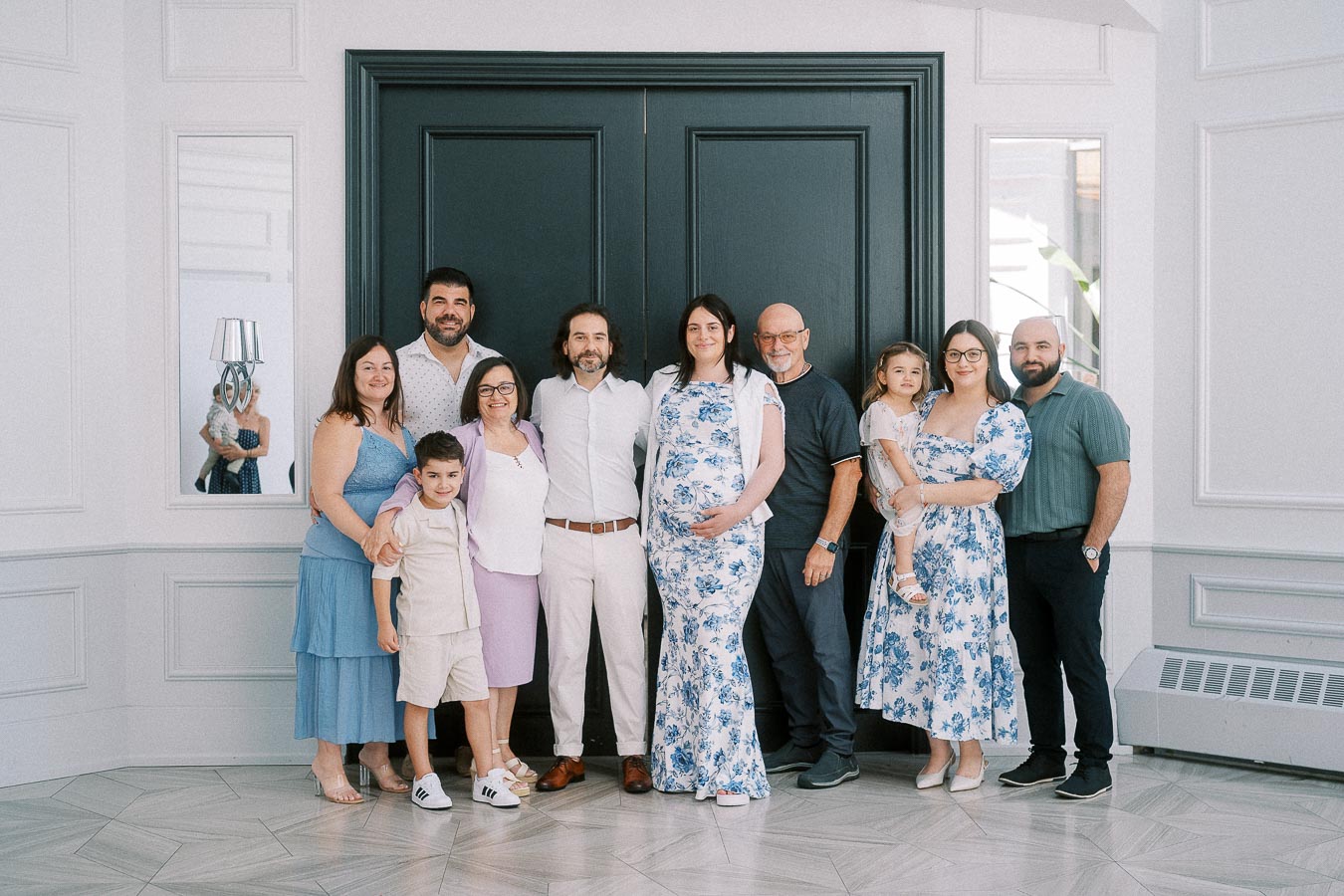 Family group portrait with pregnant woman in floral dress by dark double doors