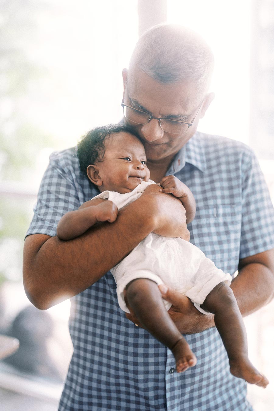 Terence cradles baby Isabella in soft window light at home in Toronto.