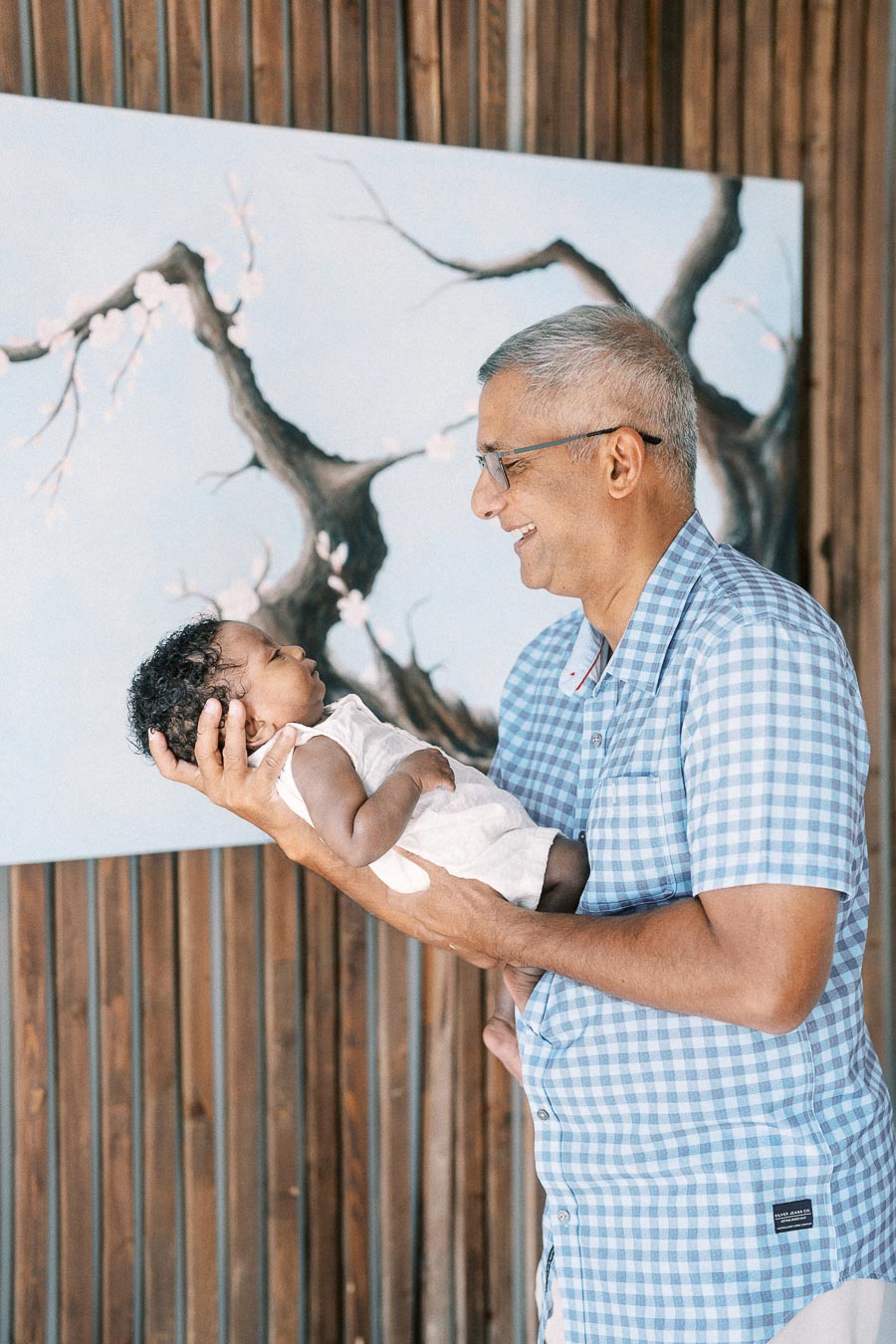 Family member smiling while holding baby Isabella against wood panelling and a blossom painting.