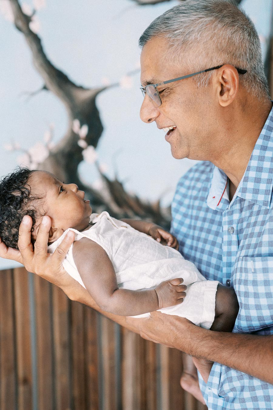 Family member smiling at baby Isabella while holding her against a tree mural.