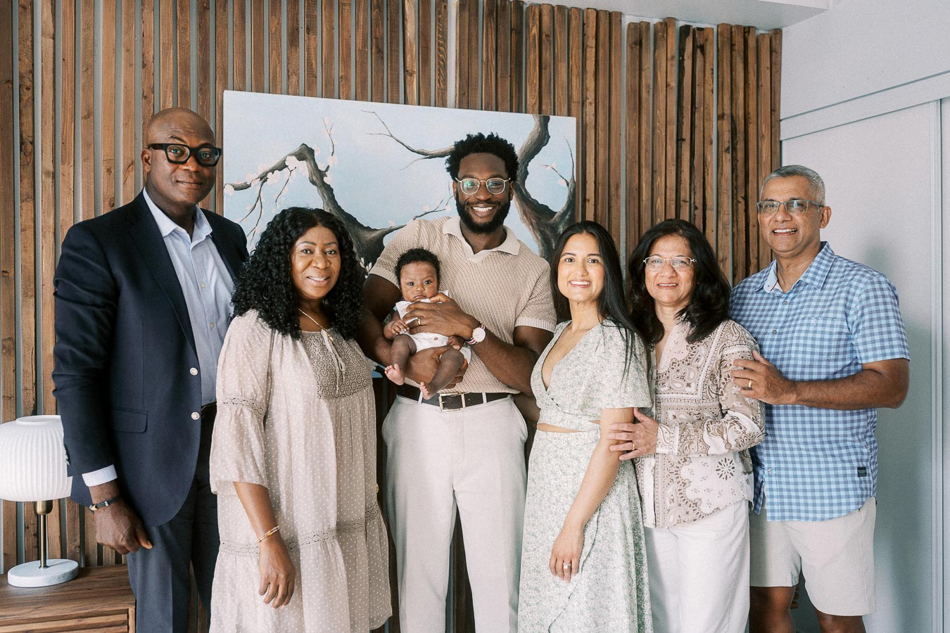 Family members gather around baby Isabella in a Toronto home with a wood slat wall.