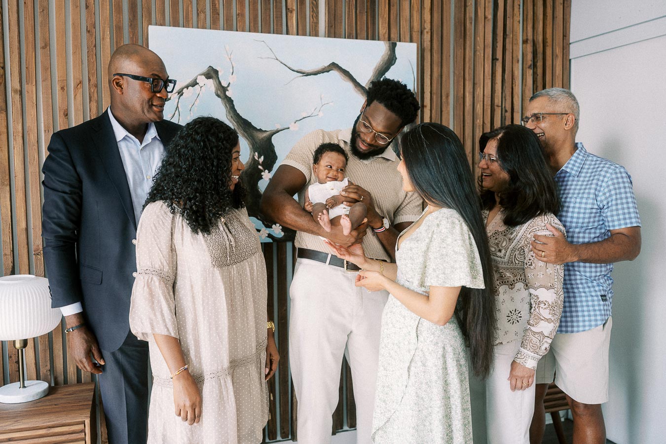 Family members gather around newborn Isabella in a Toronto home with wood slat walls.