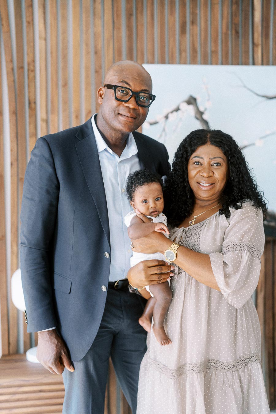 Parents Karina and Terence hold baby Isabella in front of a wood slat wall.