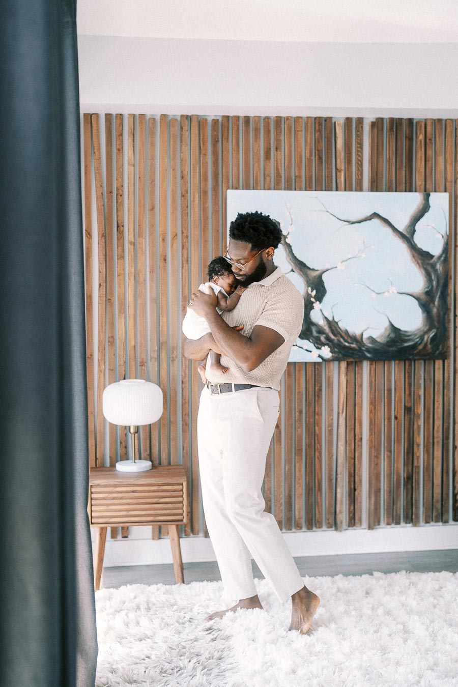 Father cuddling newborn daughter against a wood slat wall in their Toronto home