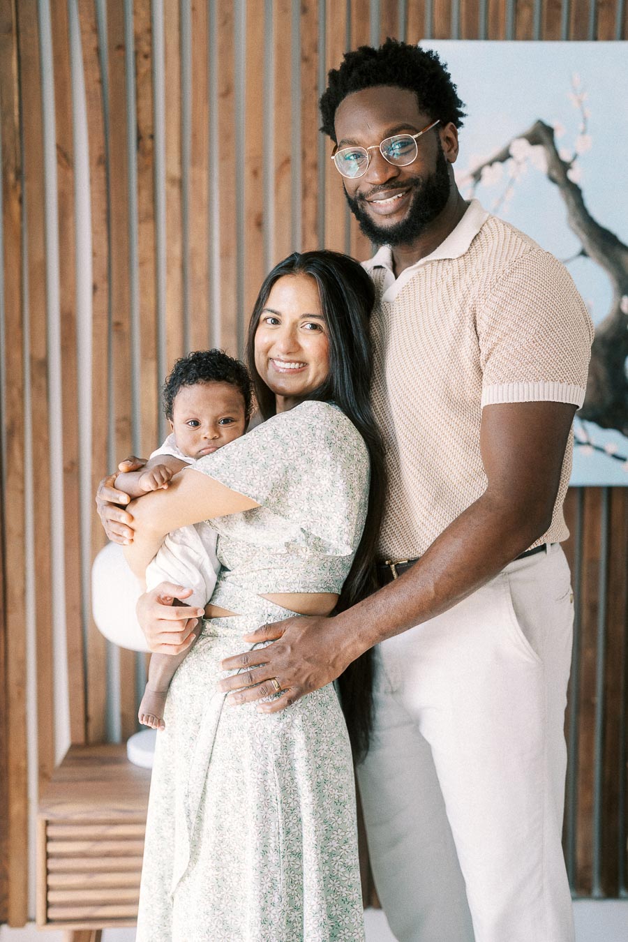 Karina and Terence holding baby Isabella beside a wood slat wall in their Toronto home.
