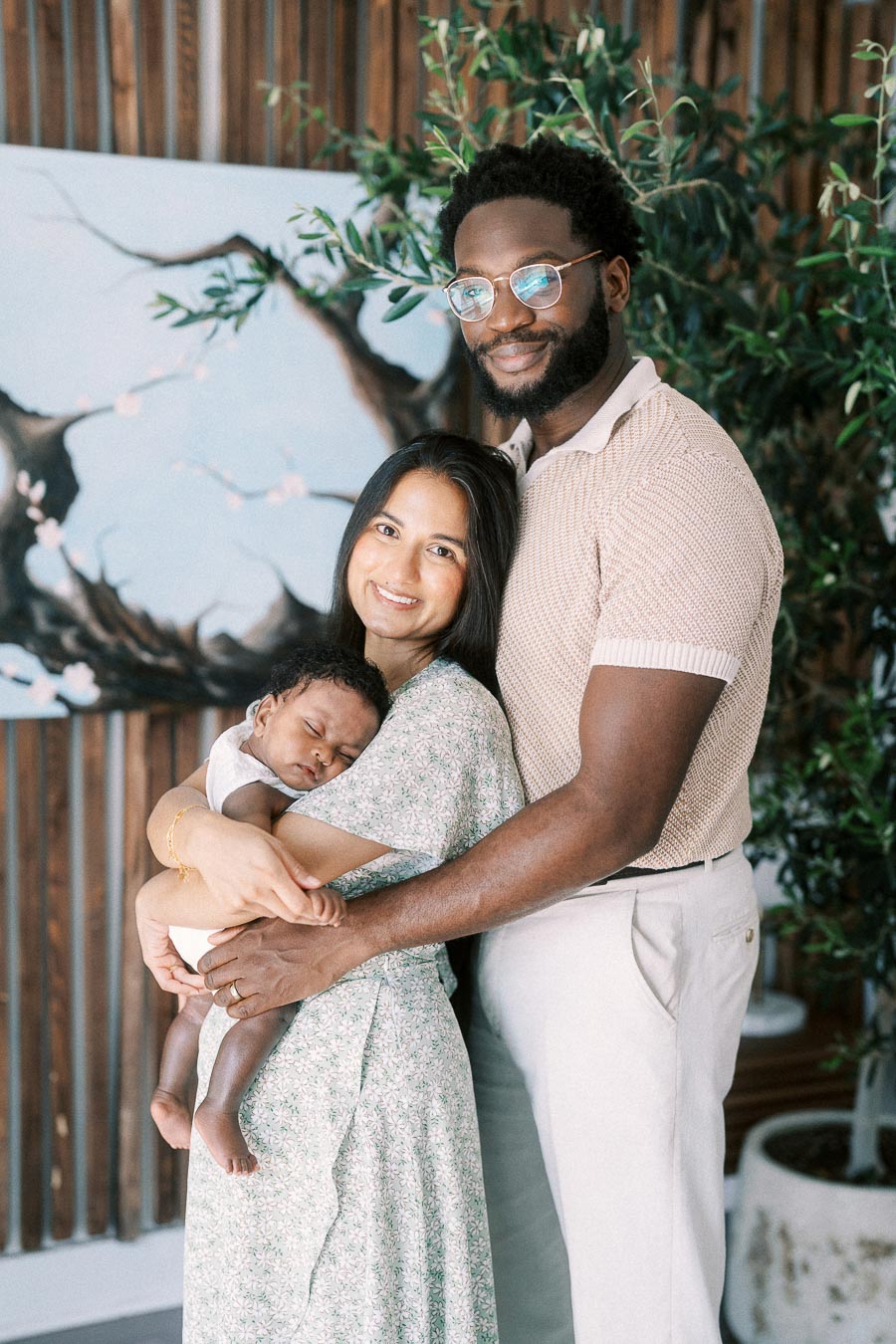 Karina and Terence hold sleeping Isabella beside indoor greenery in their Toronto home.
