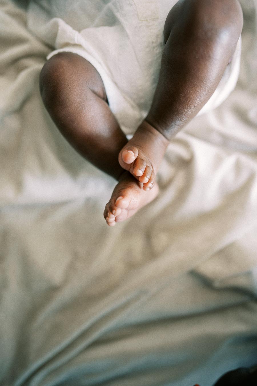 Newborn Isabella’s tiny crossed feet resting on soft bedding.