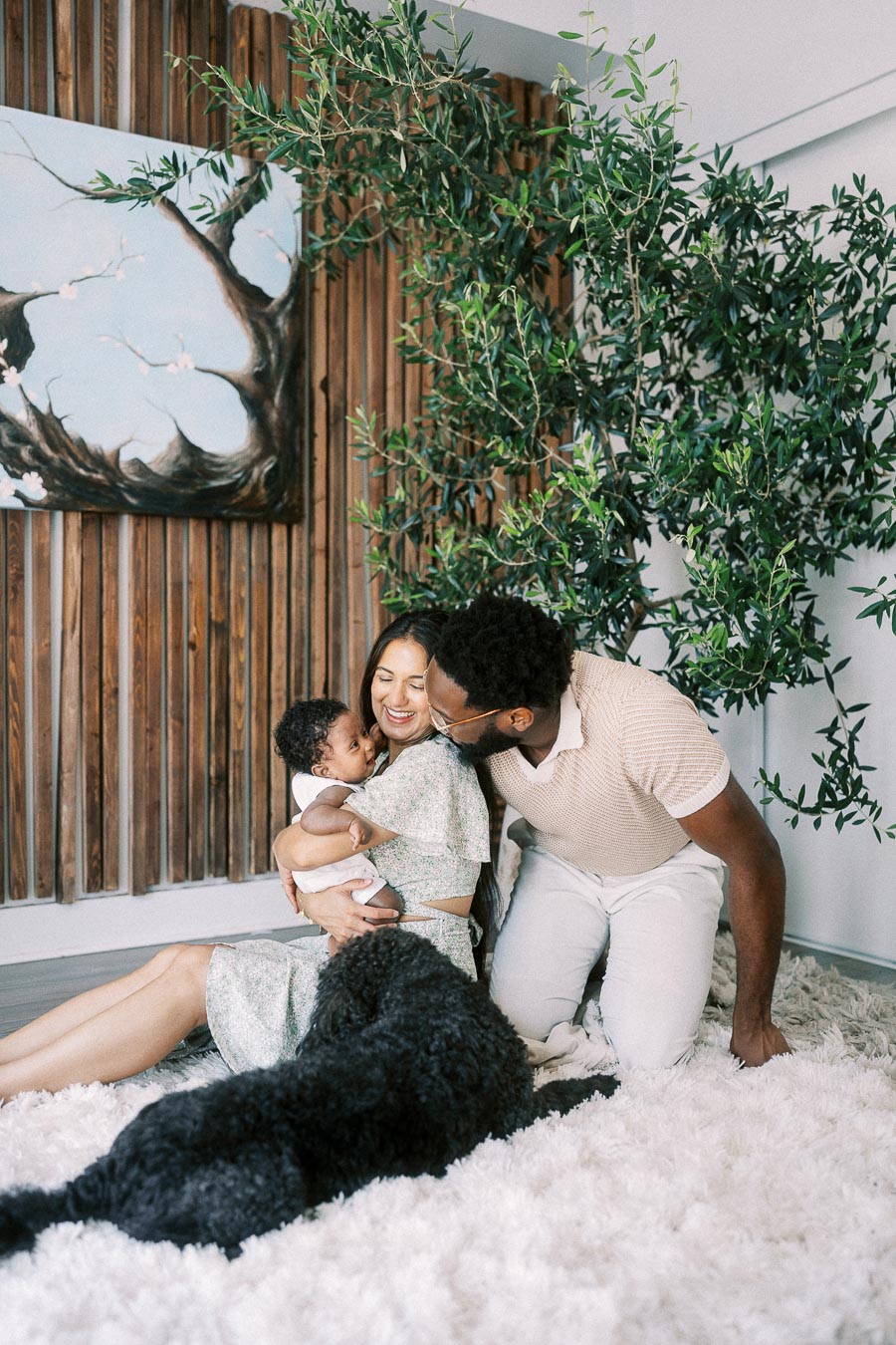 Karina holds baby Isabella as Terence leans close, with their black dog nearby.