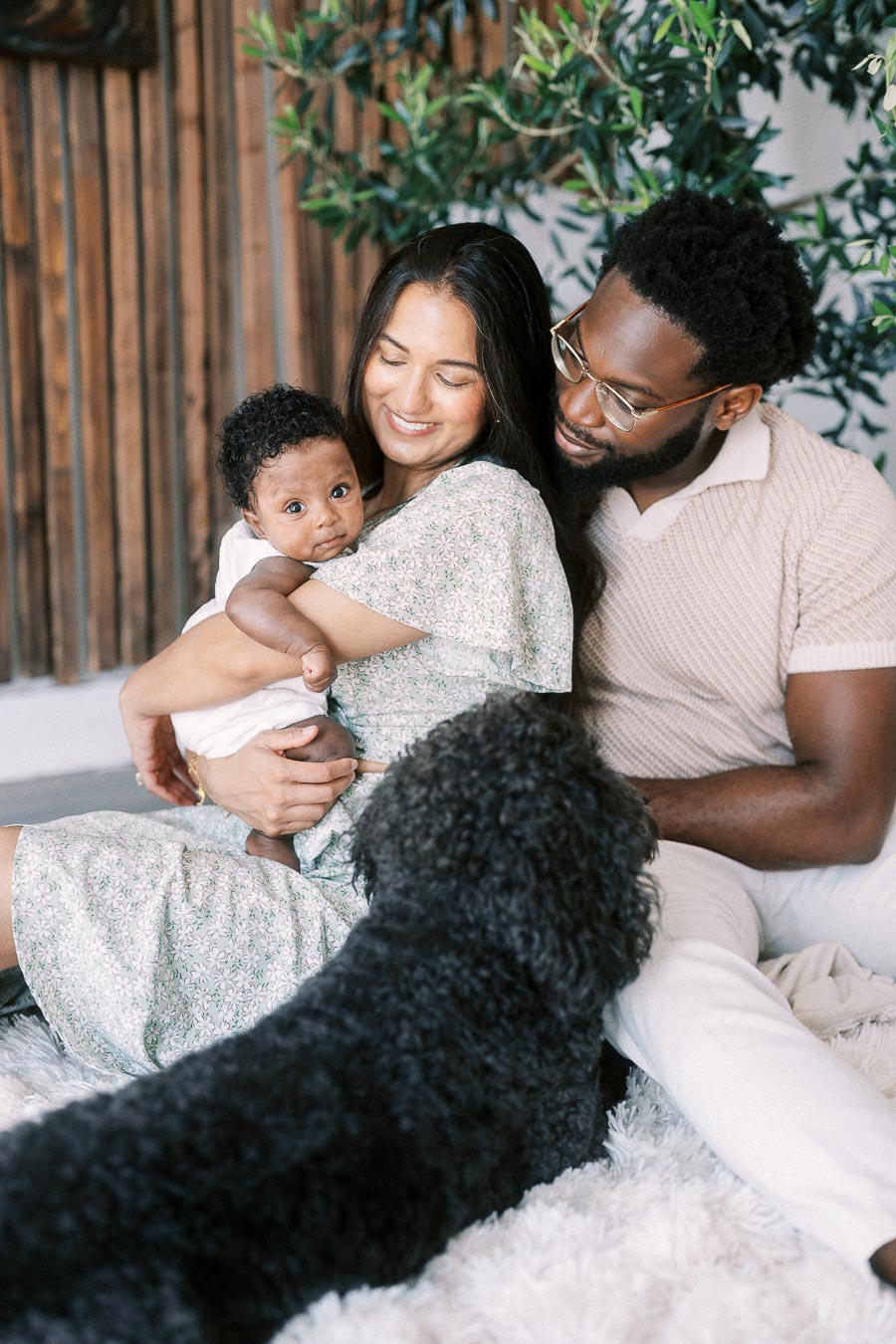 Karina holds Isabella as Terence sits beside them and their black dog stands in front.