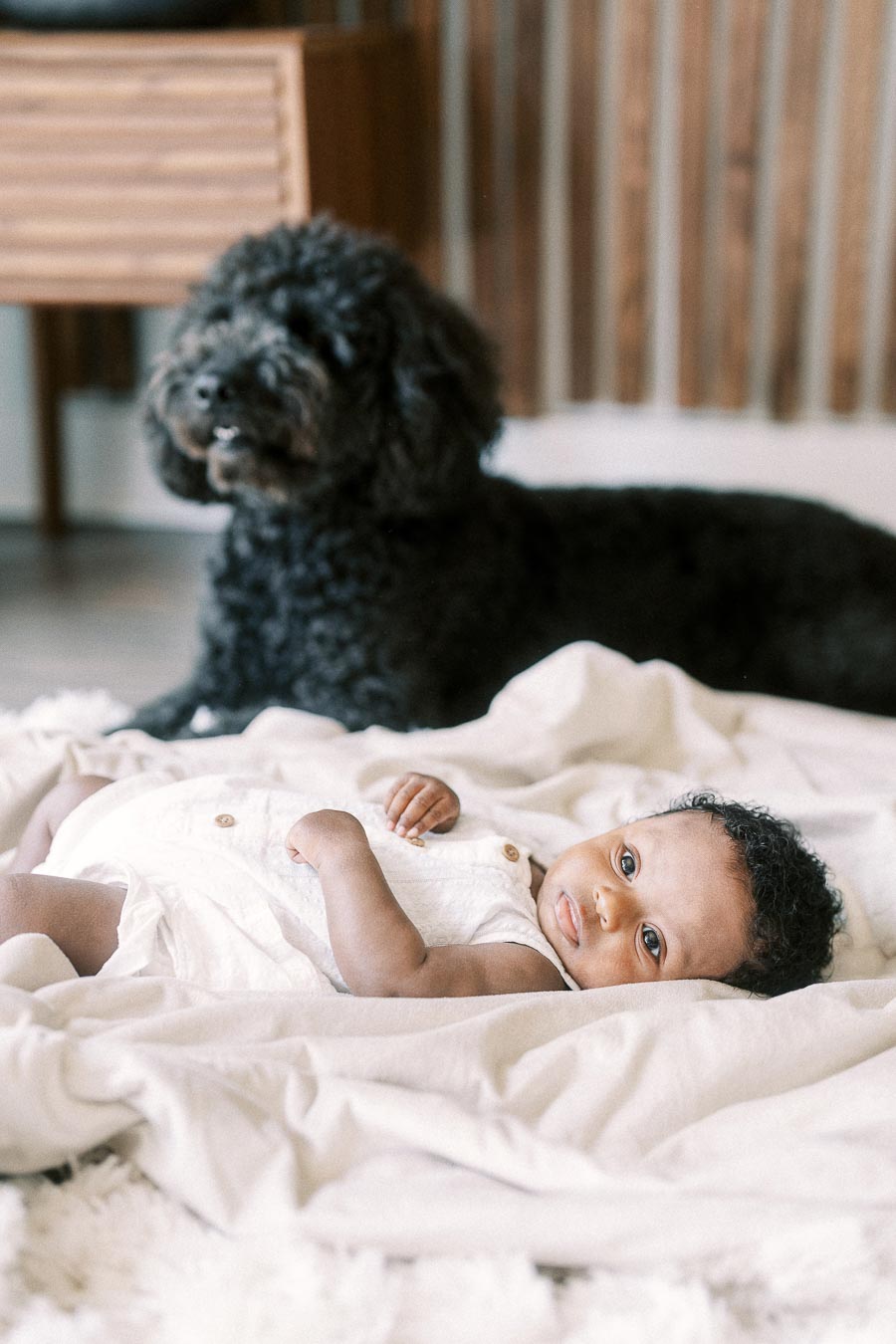 Isabella lying on a white blanket with a black family dog resting behind her.
