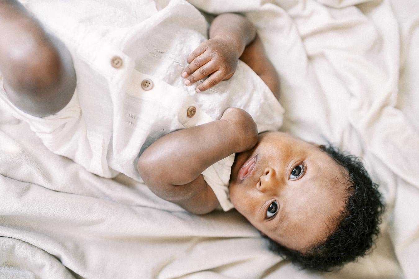 Baby Isabella lying on a cream blanket in a white buttoned outfit