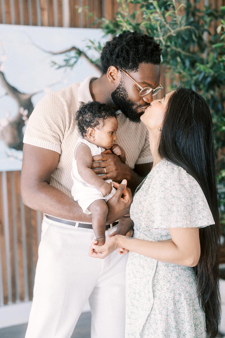 Parents kiss while holding baby Isabella during their Toronto newborn session at home.