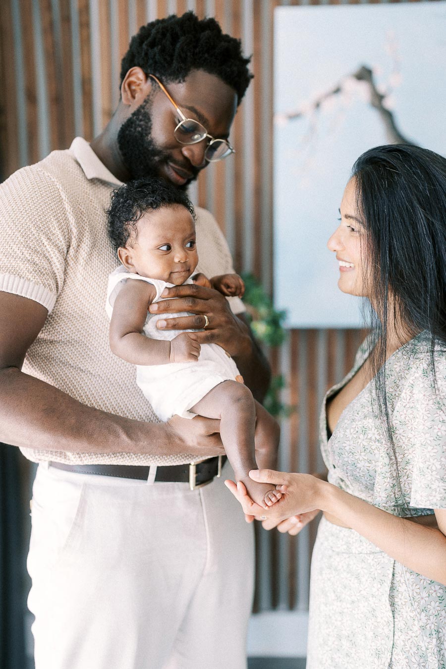 Terence holds Isabella while Karina smiles and touches her foot at home.