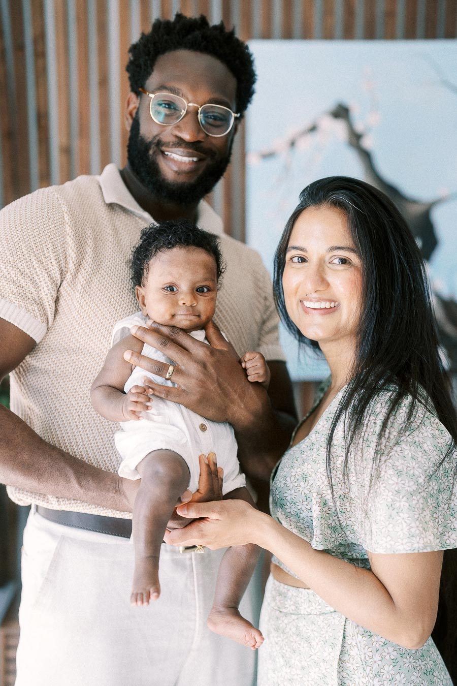 Karina and Terence hold baby Isabella at home beside wood slat wall art.