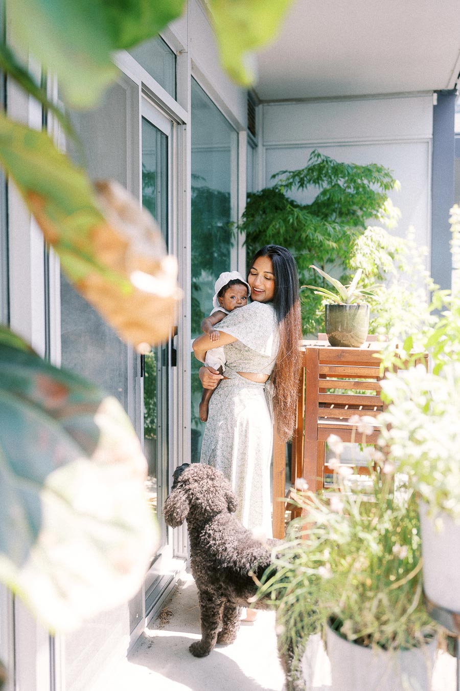 Karina holds newborn Isabella on a leafy Toronto balcony while the family dog stands nearby.