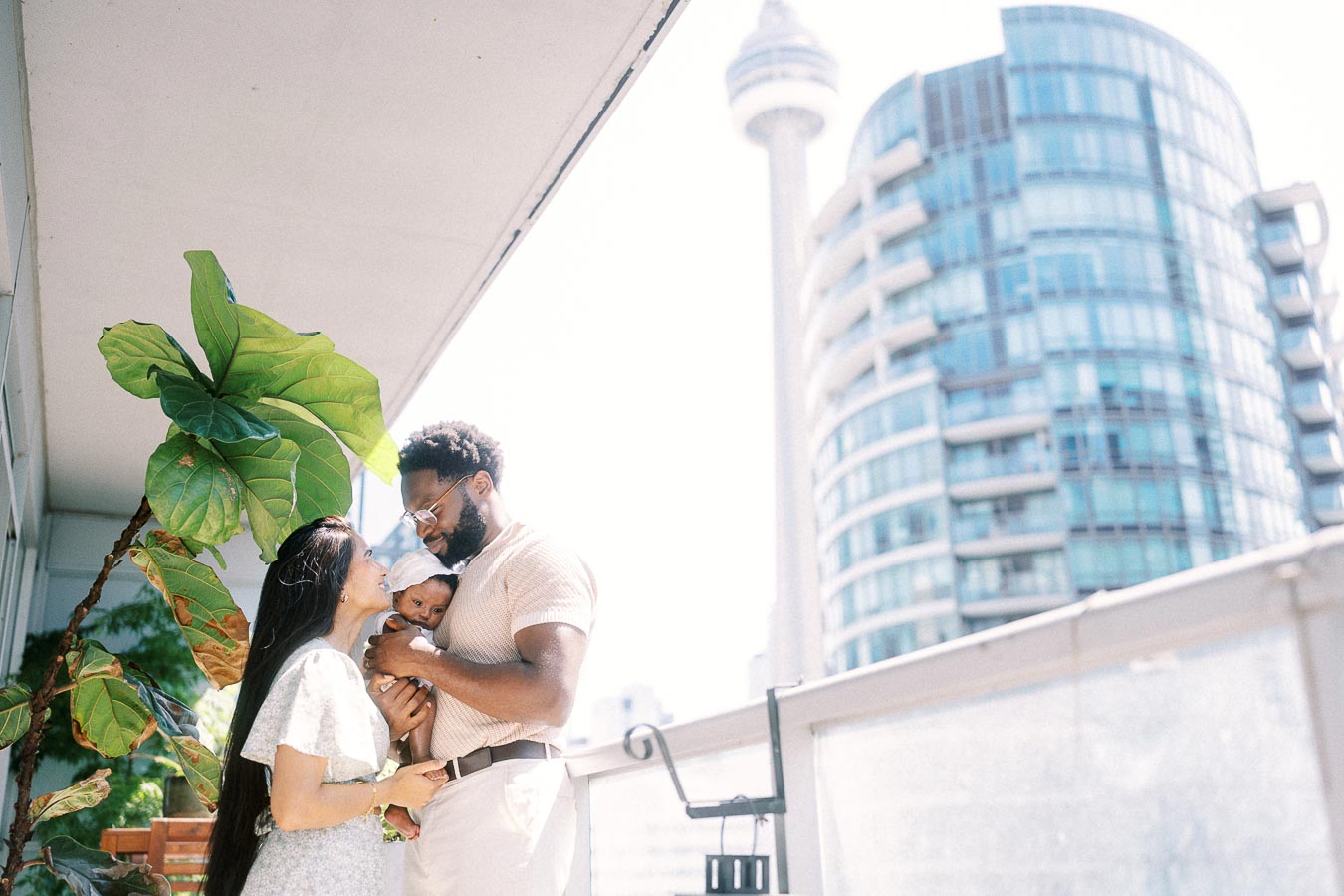 Karina and Terence cuddle Isabella on a balcony with the Toronto skyline behind them.
