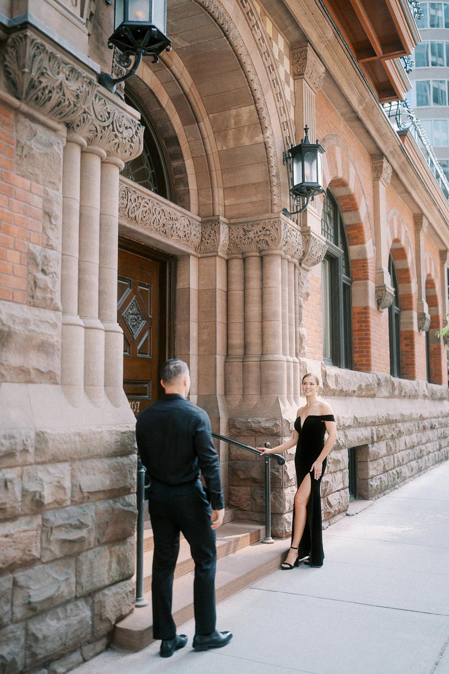 Couple in black formalwear posing outside an ornate historic stone building in downtown Toronto