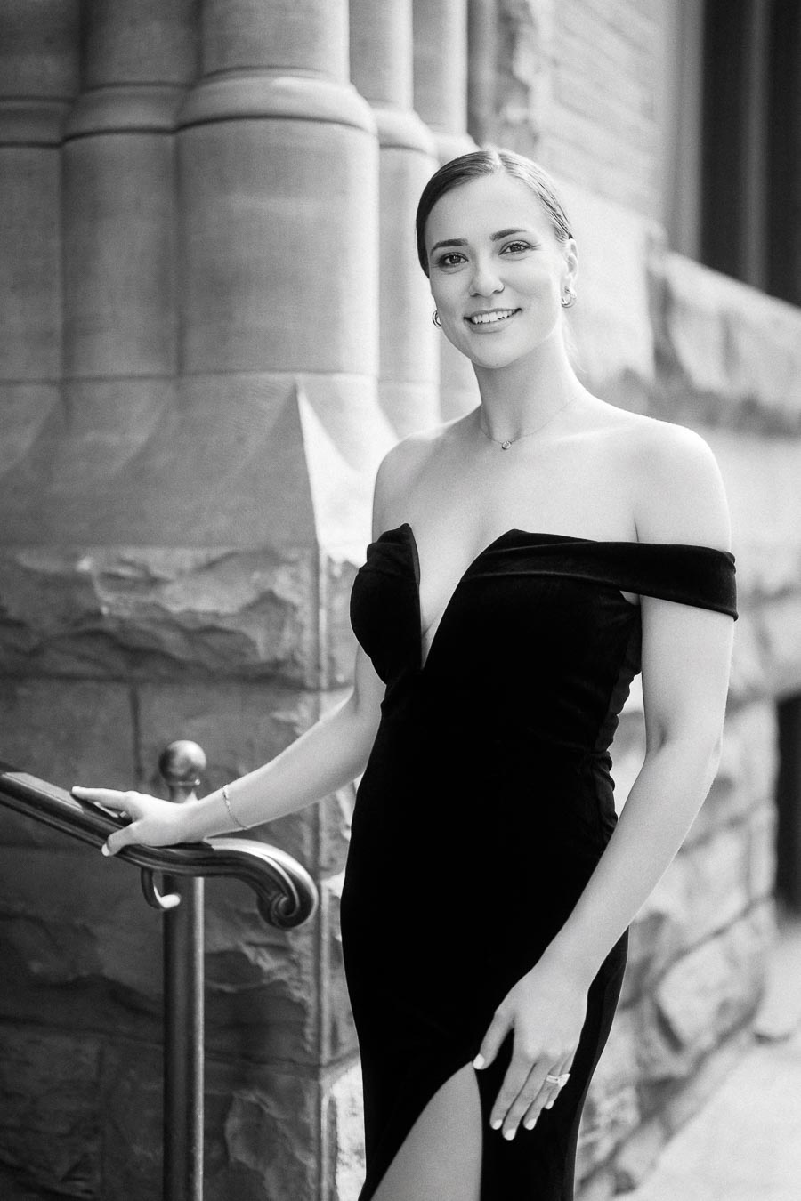Woman in an off-shoulder black gown posing by a stone entrance railing in Toronto