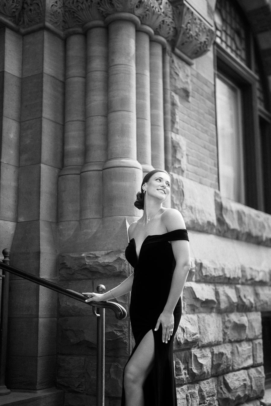 Woman in an off-shoulder black gown posing by ornate stone columns and a railing