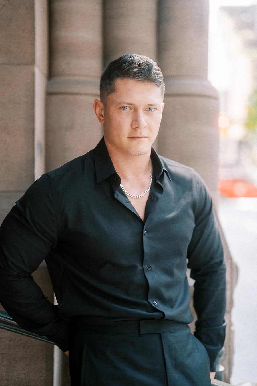 Groom-to-be in a black shirt poses beside stone columns in downtown Toronto.