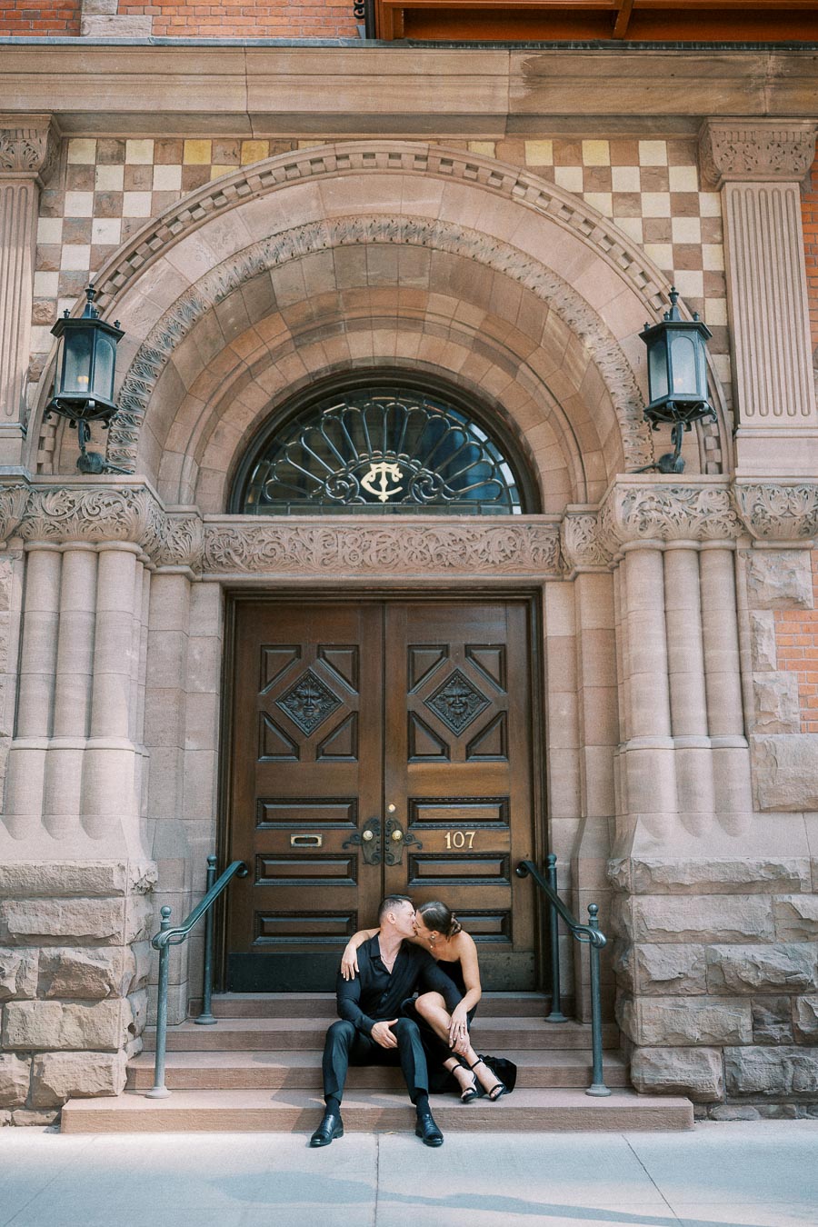 Couple kissing on stone steps beneath an ornate arched doorway in downtown Toronto.