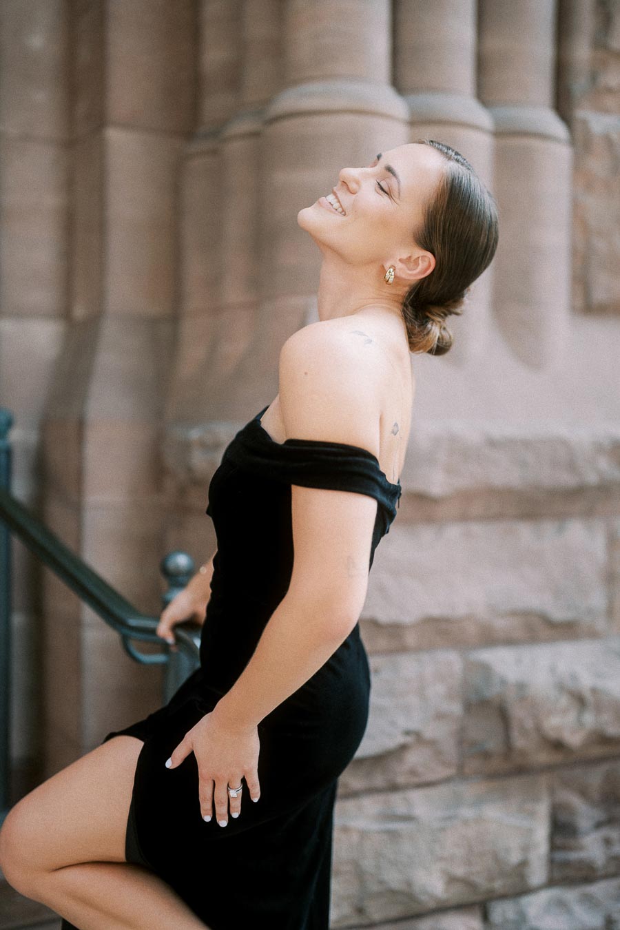 Smiling woman in a black dress poses on stone steps beside carved columns.