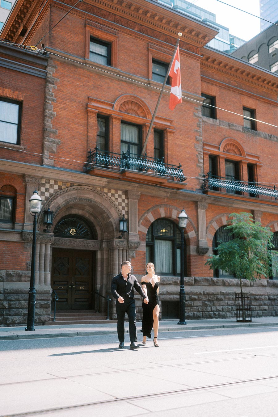 Couple holding hands outside the red brick Toronto Club building with Canadian flag above.