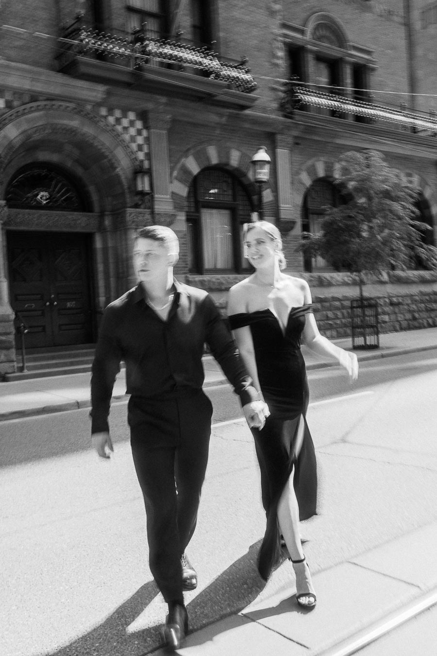 Couple holding hands while walking past an ornate stone building in downtown Toronto.