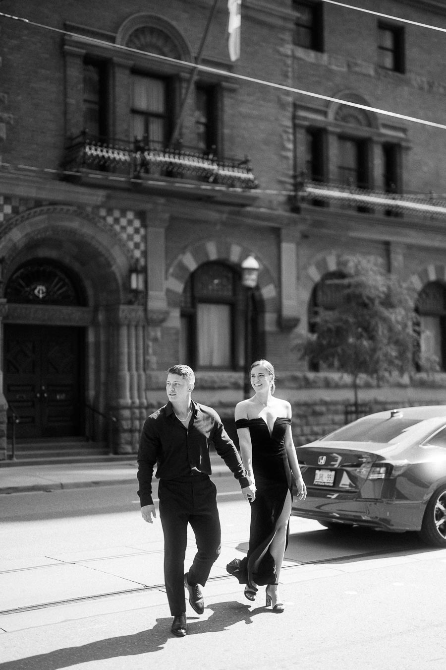Couple holding hands while crossing a downtown Toronto street in elegant black attire.