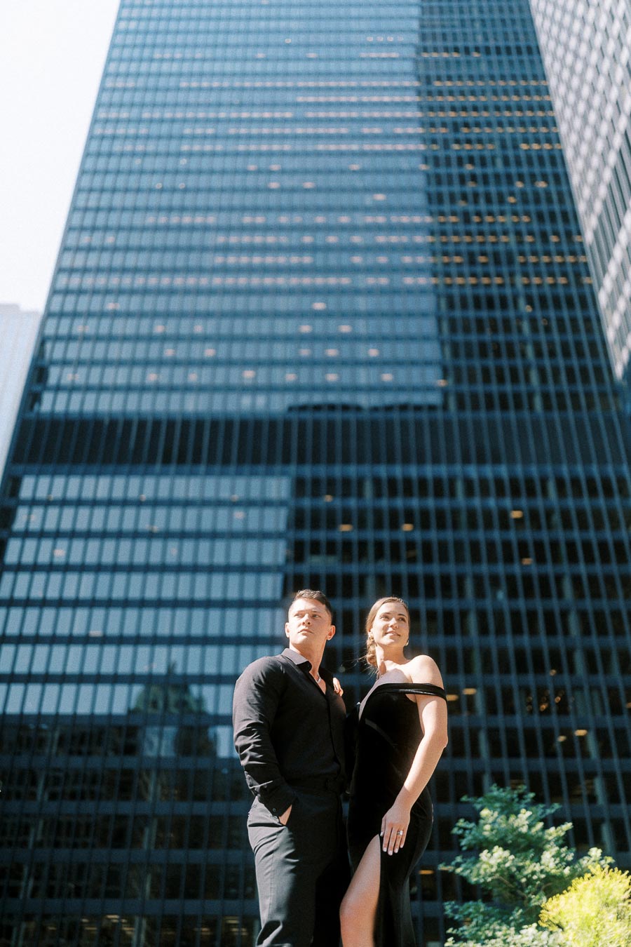 Couple in black formal outfits standing before tall glass office towers in downtown Toronto