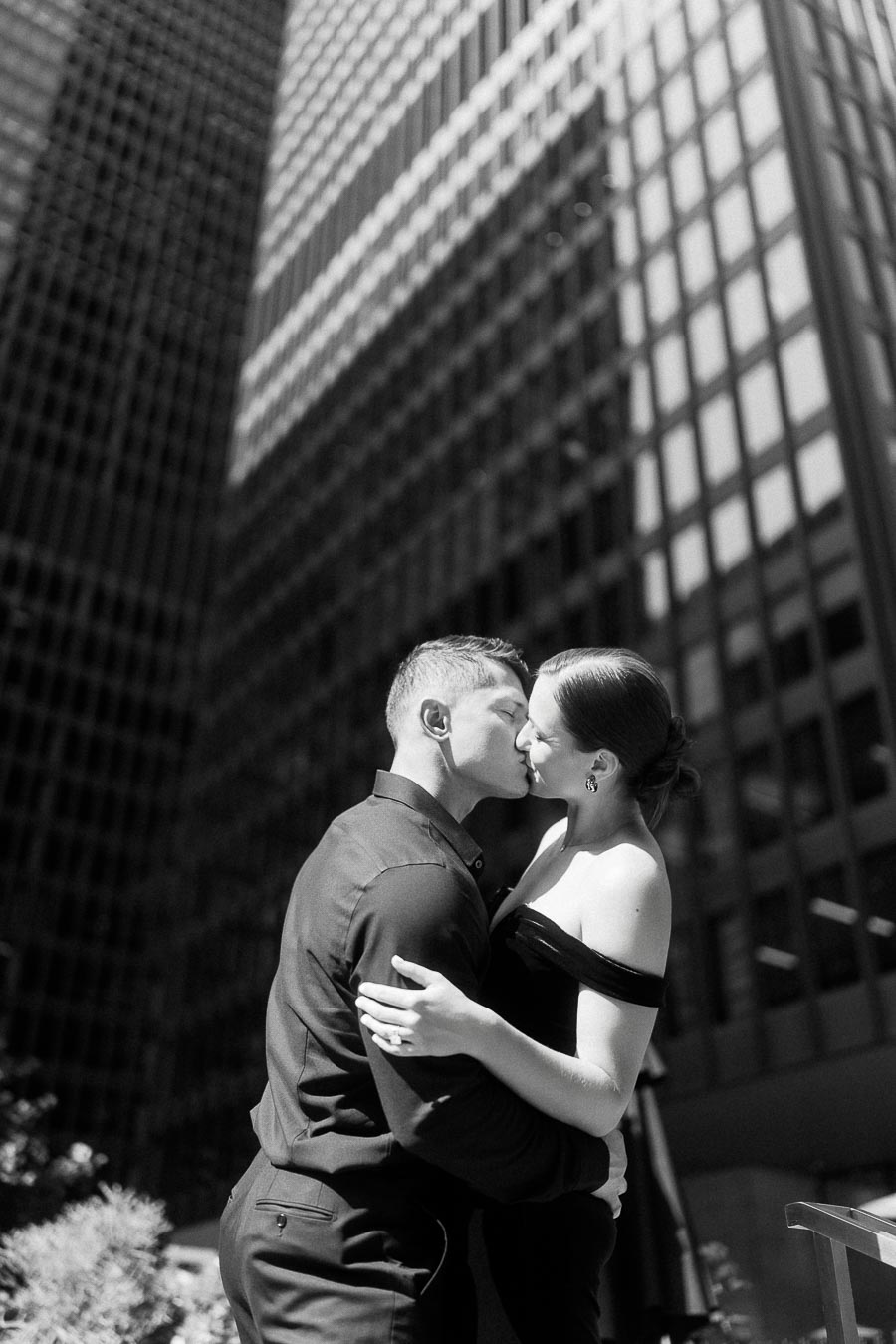 Couple kissing between tall office towers in downtown Toronto, captured in black and white.
