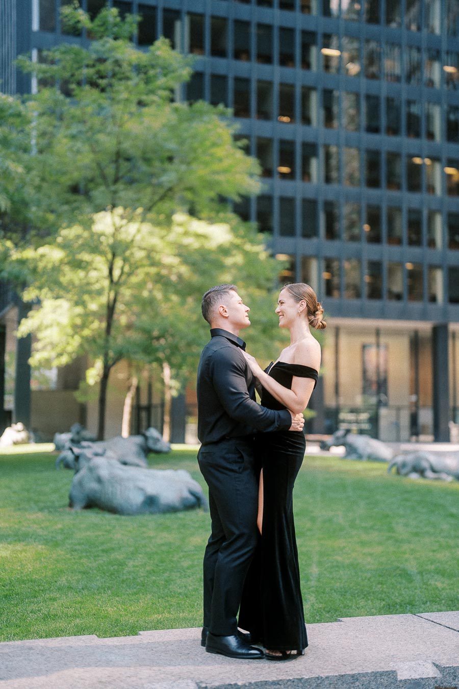 Couple in black formal attire embracing on a downtown Toronto lawn beside modern office towers.