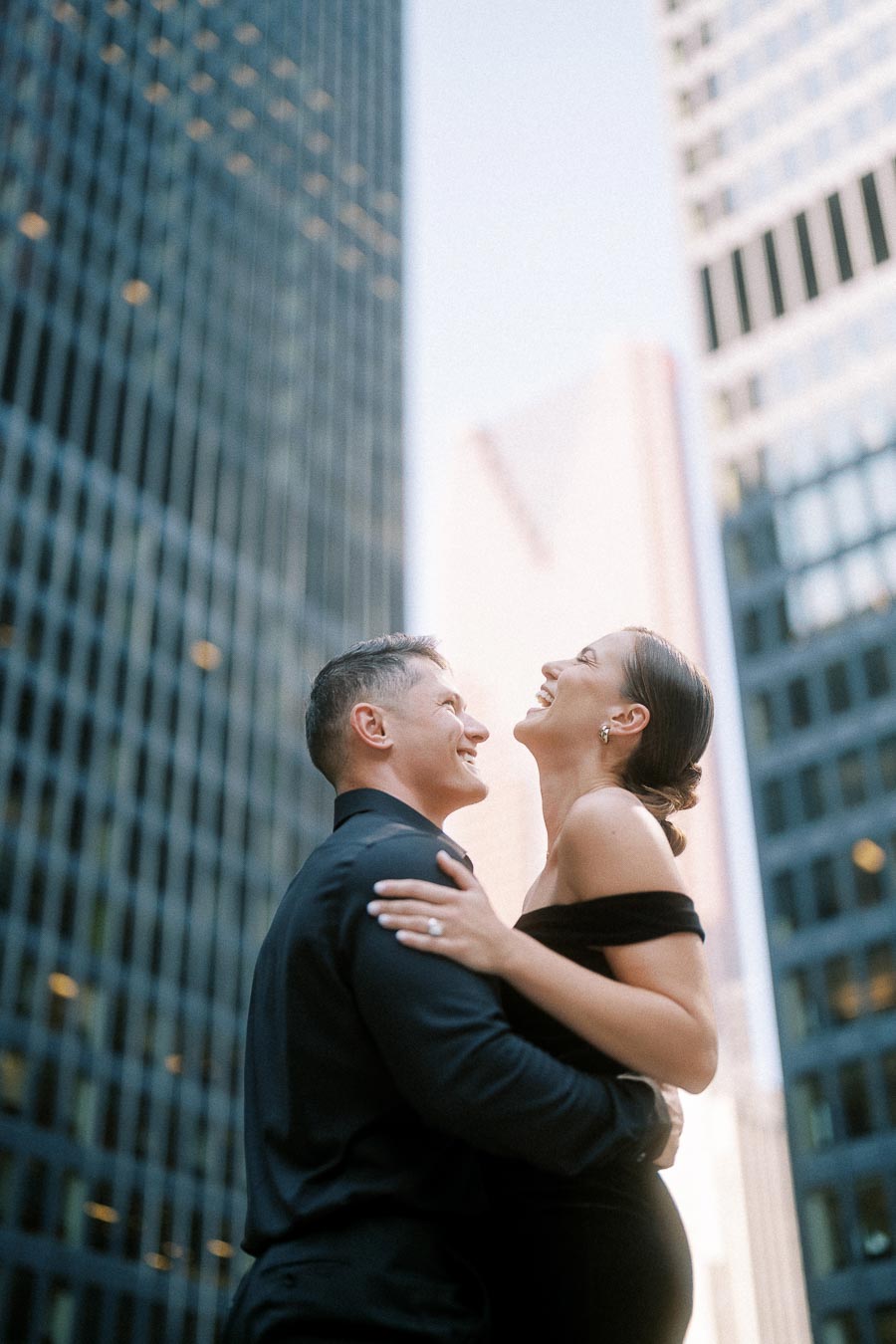 Couple in black formalwear laughing together between downtown Toronto office towers.