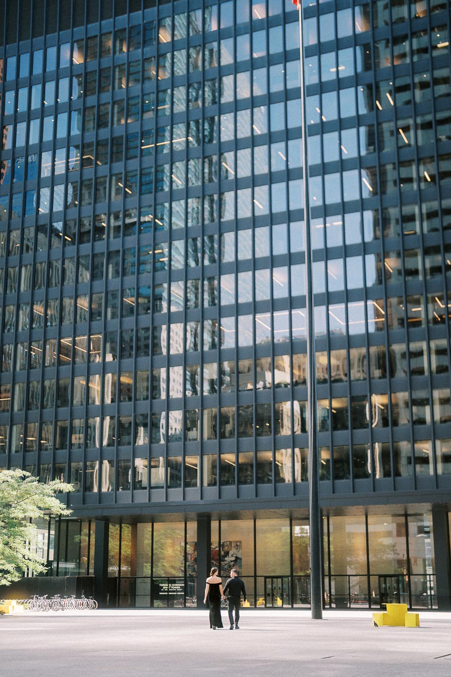 Couple walking across a downtown Toronto plaza in front of a reflective glass office tower.