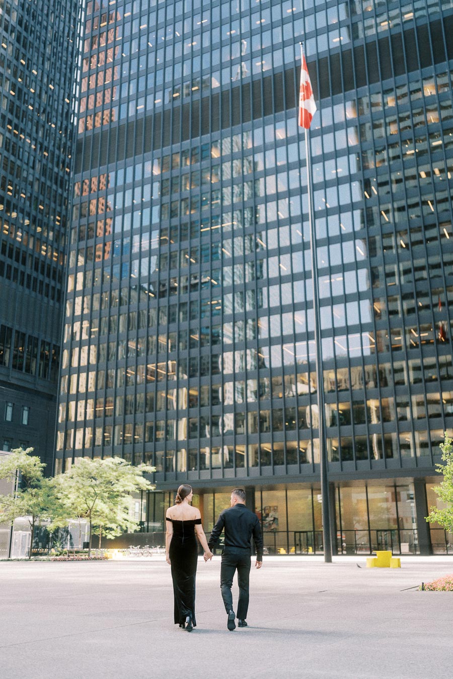 Couple walking hand in hand beneath glass office towers and a Canadian flag in downtown Toronto