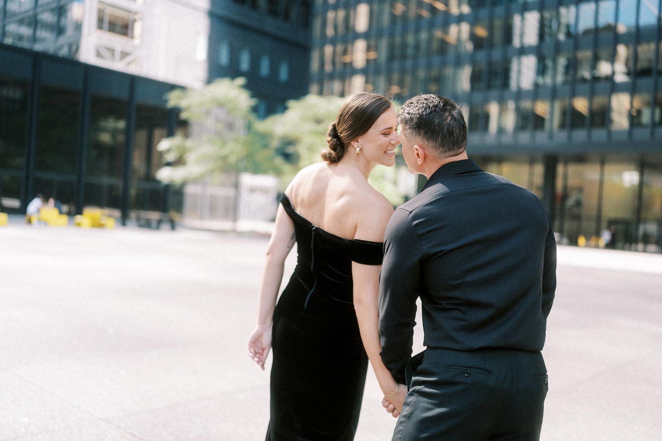 Couple holding hands and smiling while walking between glass towers in downtown Toronto.