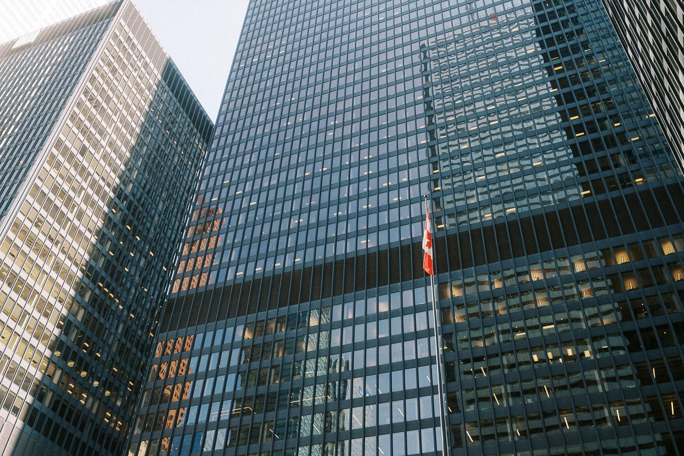 Tall glass office towers in downtown Toronto with a Canadian flag rising between them.