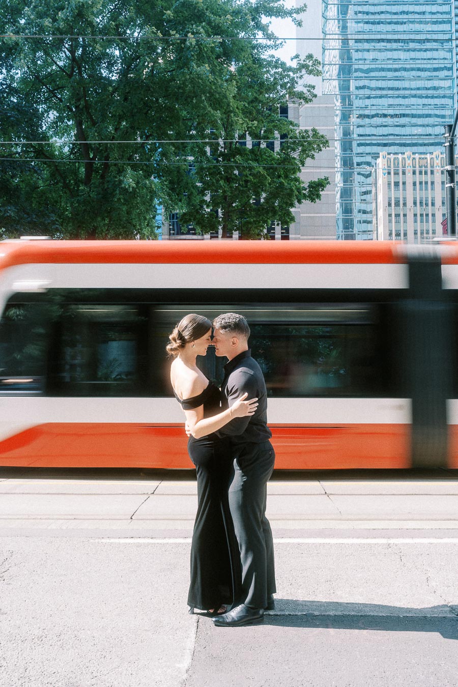 Couple in black formalwear embracing on a Toronto street as a streetcar blurs behind them.