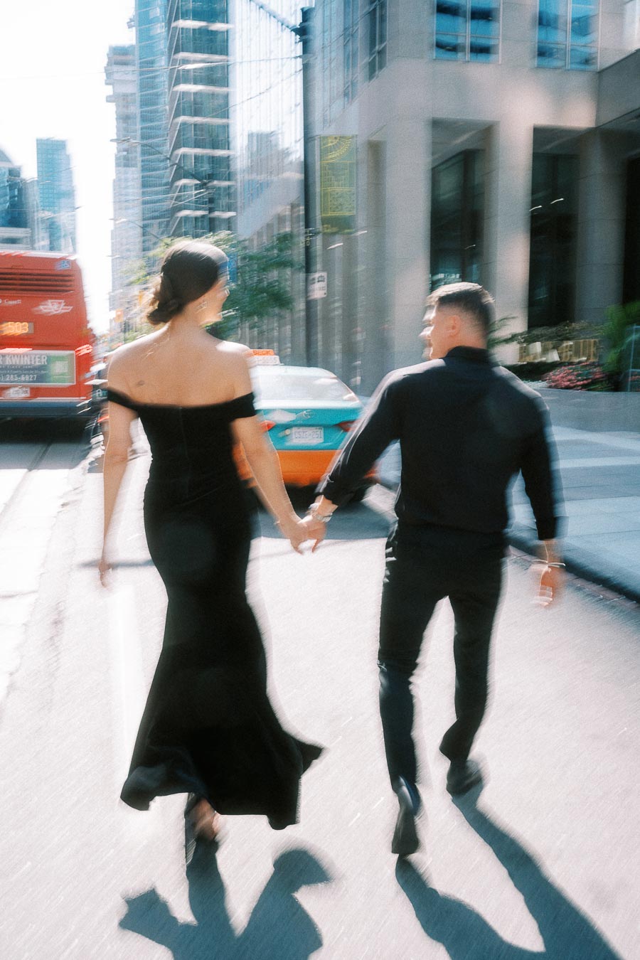 Couple in black outfits holding hands while crossing a busy downtown Toronto street