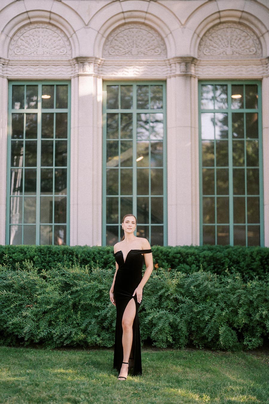 Woman in a black gown standing on grass before tall arched windows and greenery in Toronto.