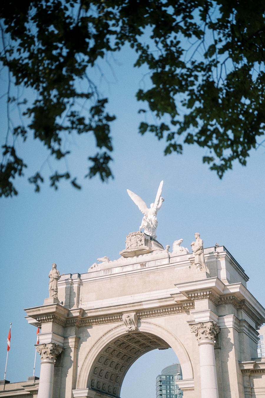 Princes' Gates arch at Exhibition Place framed by leafy branches against a clear blue sky