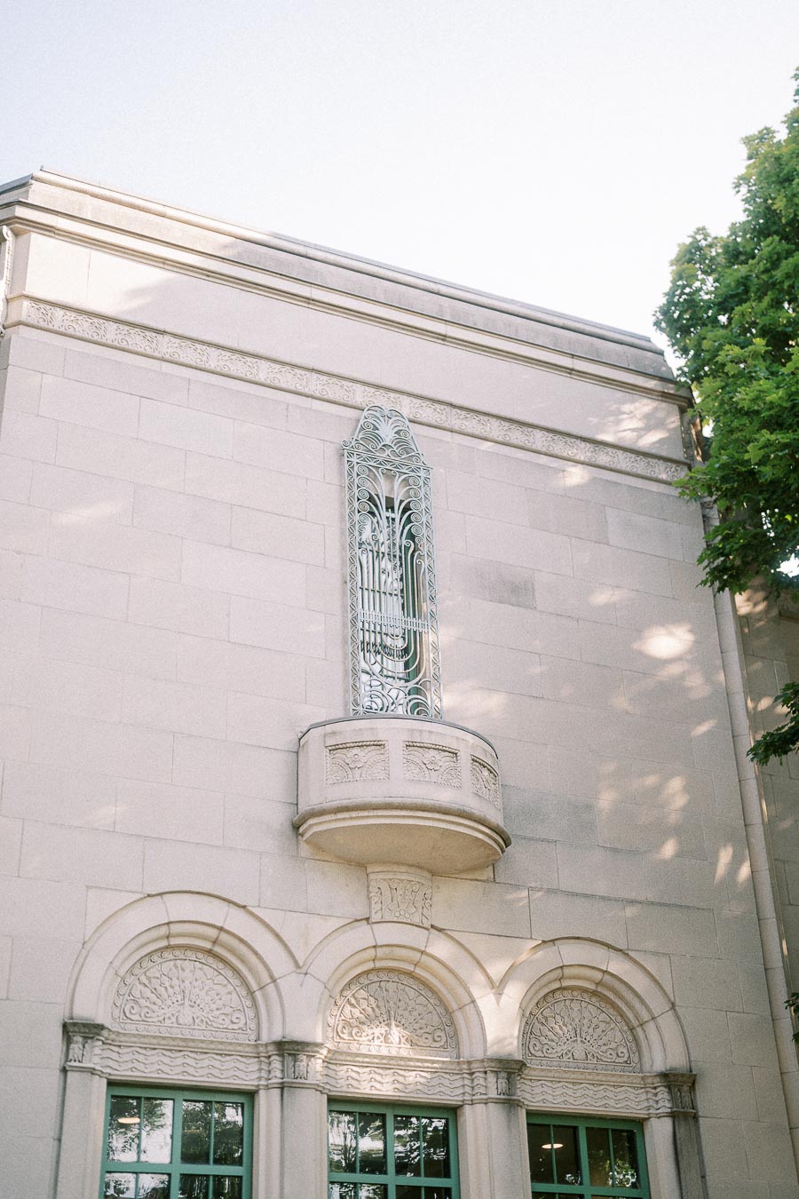 Ornate stone façade with arched windows, green frames, and a small decorative balcony in Toronto.