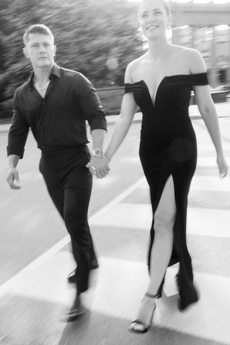 Couple holding hands while crossing a city street in formal black outfits with motion blur.
