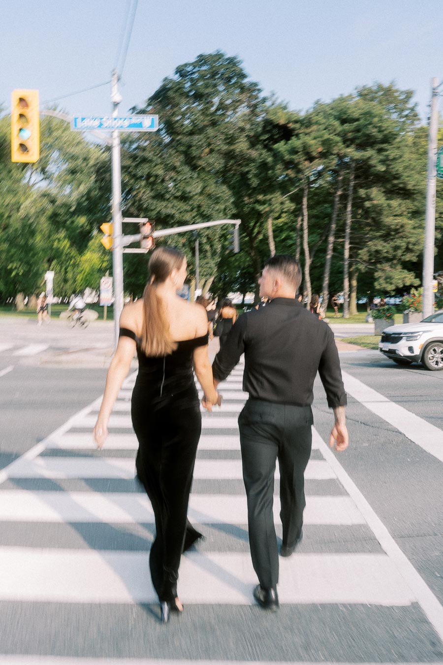 Couple in black outfits holding hands while crossing a Toronto street at a marked crosswalk.
