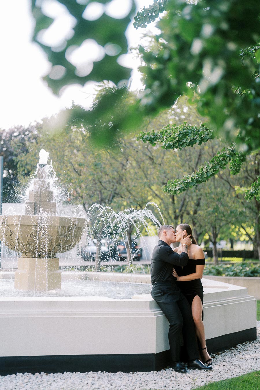 Couple kissing beside a garden fountain with trees and greenery in downtown Toronto.