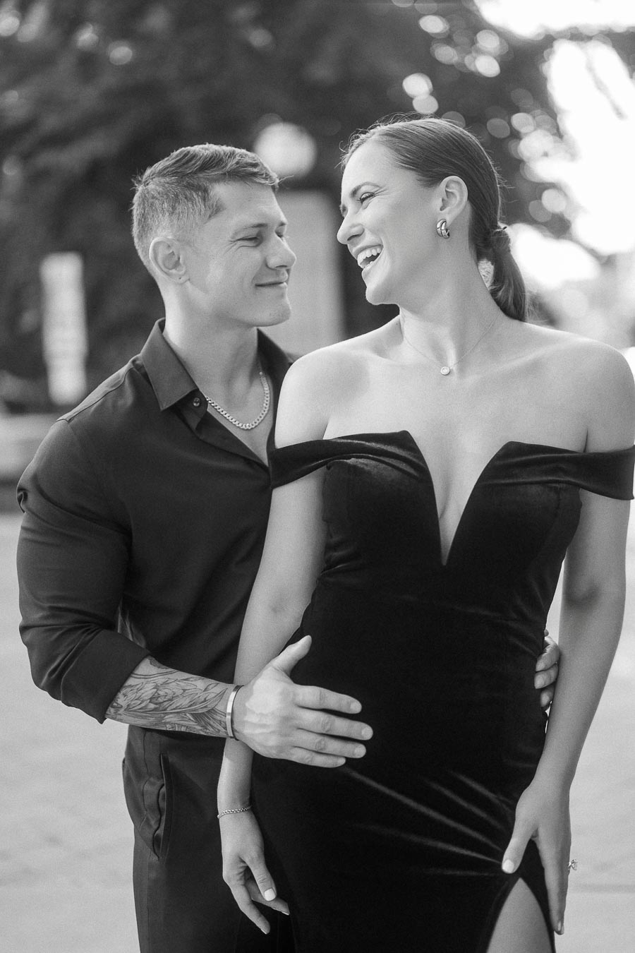 Couple laughing together in elegant black outfits during an outdoor Toronto engagement portrait.