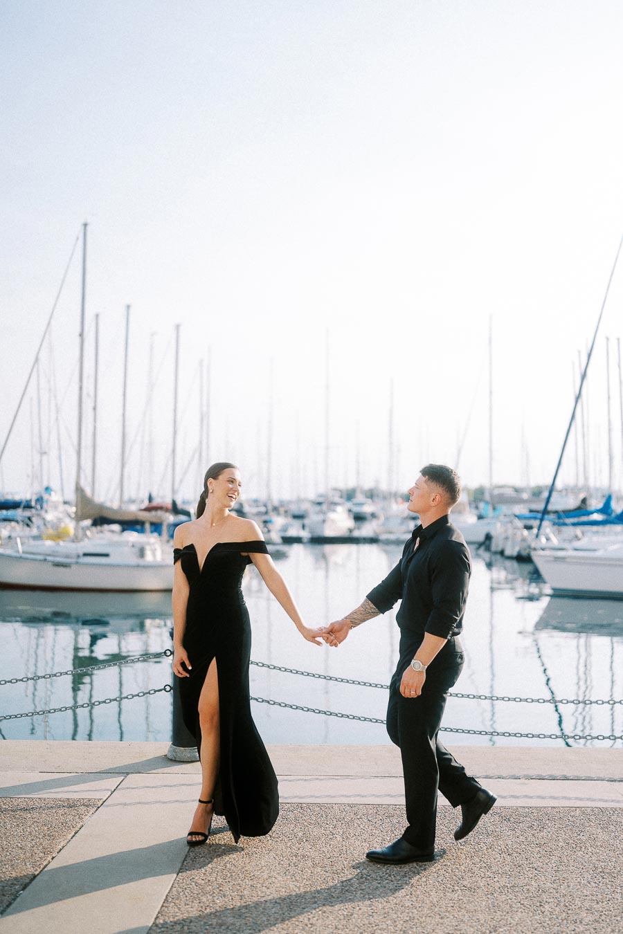 Couple in black formalwear holding hands beside sailboats at a Toronto waterfront marina